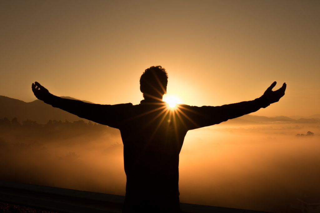 The silhouette of a man standing in a brilliant sunset with his arms stretched out on each side in worship.